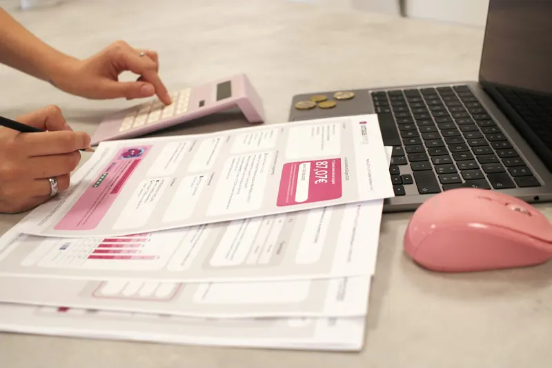 Hands sorting bills next to a calculator and laptop