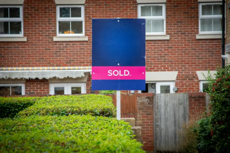 A blue SOLD sign in front of a brick house